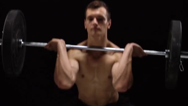 Man doet oefeningen met een barbell, is betrokken bij een crossfit op een zwarte achtergrond in de studio — Stockvideo