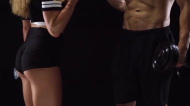 Atletik erkek ve kadın şişiriyor dambıl, kendi elleriyle kendi pazı Studio siyah bir zemin üzerine eğitim