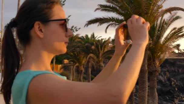 Mujer tomando fotos de la puesta de sol en el paseo marítimo, Tenerife, Islas Canarias, España — Vídeo de stock