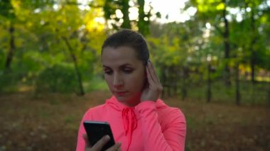 Kadın bir akıllı telefon ve kablosuz kulaklık ile müzik seçer ve sonbahar Parkı ile çalışır
