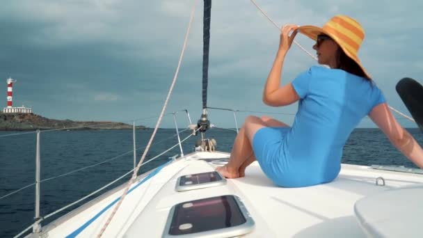 Жінка в жовтому капелюсі і синьому платті лежить на яхті біля маяка в літній сезон в океані. Повільний рух — стокове відео