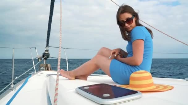 Mujer con un sombrero amarillo y vestido azul descansa a bordo de un yate en la temporada de verano en el océano — Vídeo de stock