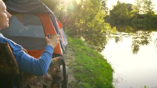 Vrouw is het drinken van thee in een fauteuil in de buurt van een tent aan de rivieroever — Stockvideo