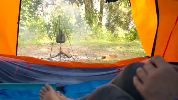 Kvinna i ett tält dricker varmt te. Vattenkokaren värms på elden framför henne — Stockvideo