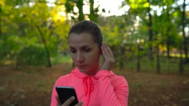Kadın bir akıllı telefon ve kablosuz kulaklık ile müzik seçer ve sonbahar Parkı ile çalışır. Ağır çekim