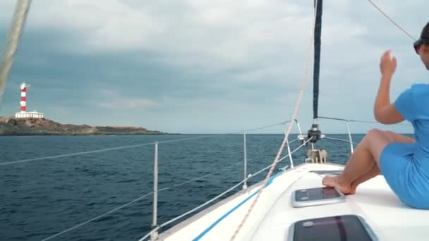 Femme au chapeau jaune et robe bleue repose à bord d'un yacht près du phare en saison estivale à l'océan — Video