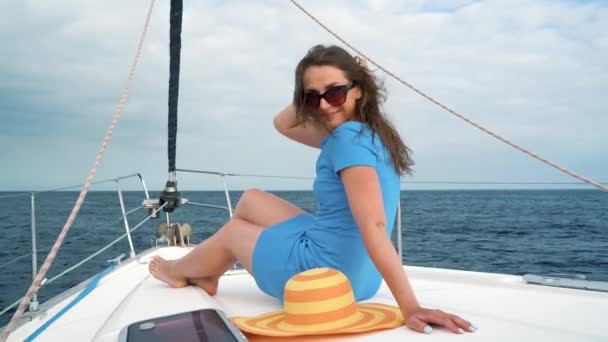 Mujer con un sombrero amarillo y vestido azul descansa a bordo de un yate en la temporada de verano en el océano — Vídeo de stock