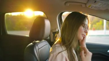 Gözlüklü güzel kız onun kulaklarına kablosuz kulaklık takılı ve sürücü hakkında onun emniyet uzak bir arabaya kemerlerinizi bağlayın