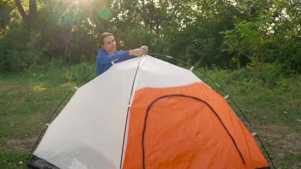 Mulher está colocando uma tenda turística na floresta ao pôr do sol — Vídeo de Stock