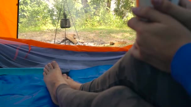 Uma mulher numa tenda bebe chá quente. A chaleira é aquecida na fogueira na frente dela — Vídeo de Stock