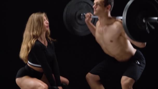 Athlétisme homme et femme accroupi avec un poids supplémentaire, l'entraînement de leurs jambes et fesses sur un fond noir en studio — Video