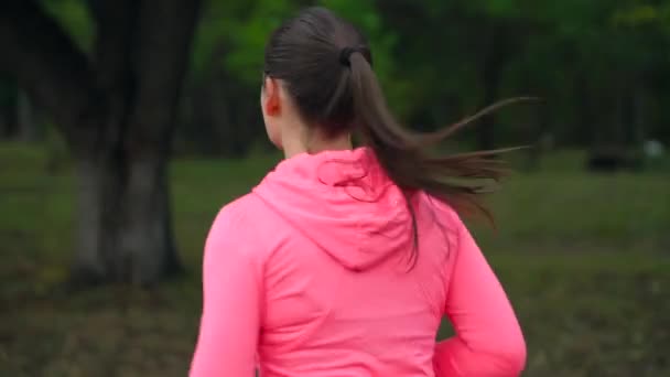 Primer plano de la mujer corriendo a través de un parque de otoño al atardecer, vista trasera. Movimiento lento — Vídeos de Stock