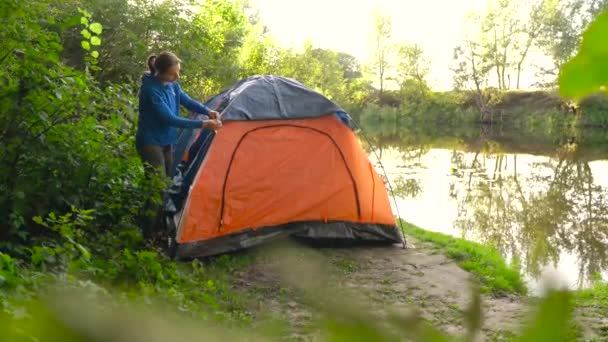 Vrouw zet een toeristische tent op de rivier bank — Stockvideo