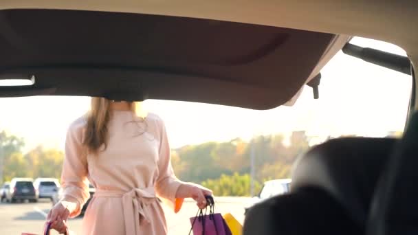 Menina bonita coloca sacos de compras no porta-malas de um carro e sai, com a intenção de ir embora. Movimento lento — Vídeo de Stock