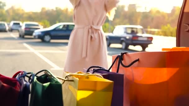 Hermosa chica recoge bolsas de la compra del maletero del coche, lo cierra y se va. Movimiento lento — Vídeos de Stock