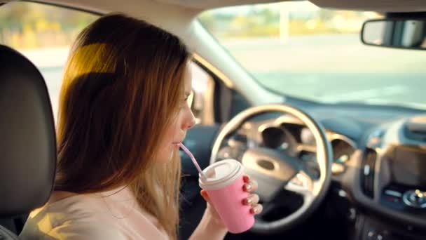 Hermosa chica alegre se sienta en el coche, bebe café y ríe — Vídeos de Stock