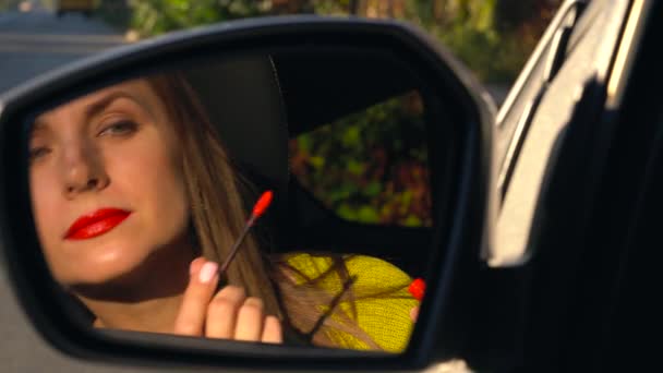 La mujer se pinta los labios con lápiz labial rojo y se mira en el espejo retrovisor — Vídeos de Stock
