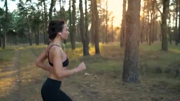 Крупный план женщины в наушниках, бегущей через осенний лес на закате. Съемка на разных скоростях - нормальная и замедленная — стоковое видео