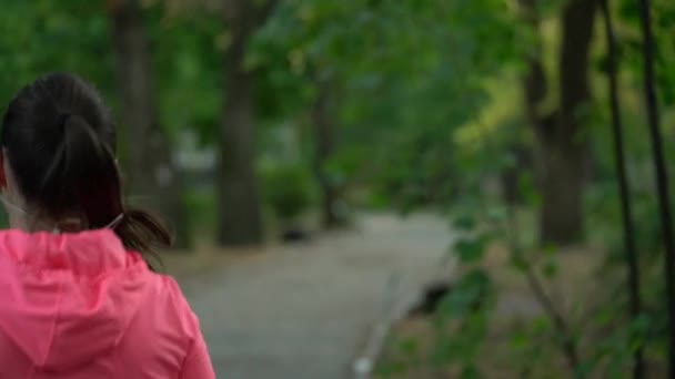 Primer plano de la mujer corriendo a través de un parque de otoño al atardecer, vista trasera . — Vídeos de Stock
