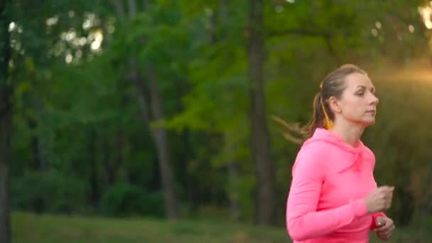 Zbliżenie kobieta działa przez jesienny park o zachodzie słońca. Zwolnionym tempie — Wideo stockowe