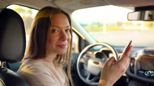 Woman using the phone while sitting in the car and talking to someone behind the scenes — Stock Video