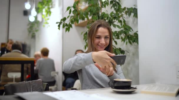 Piękna kobieta spędza czas w kawiarni: rmakes zdjęcia na portalach społecznościowych - kawy i książki — Wideo stockowe