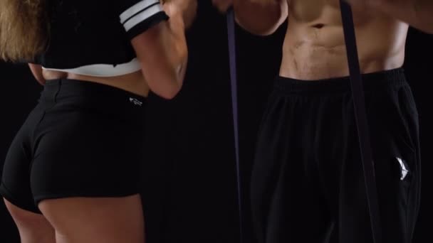 Atlético hombre y mujer haciendo ejercicio en el bíceps con bandas elásticas sobre un fondo negro en el estudio — Vídeos de Stock