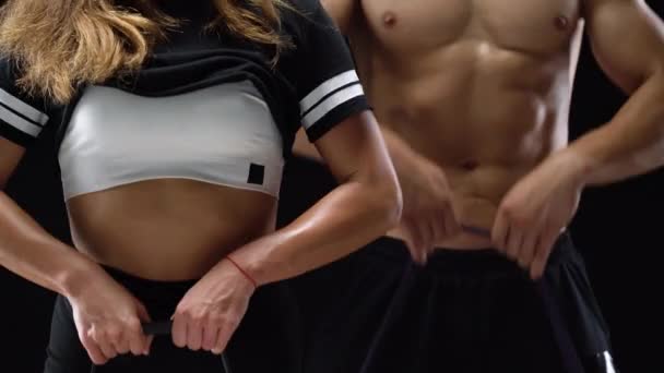 Atletický muž a žena, která dělá cvičení na ramena s elastickým pásem na černém pozadí v studio — Stock video