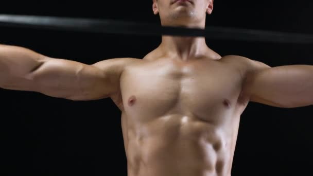 Atletisk man gör övningen på hans axlar med gummiband på en svart bakgrund i studio — Stockvideo