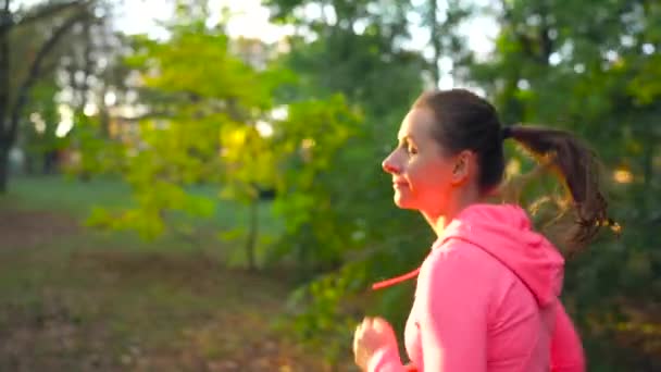 Zbliżenie kobieta działa przez jesienny park o zachodzie słońca. Zwolnionym tempie — Wideo stockowe