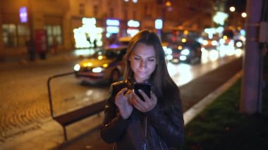 Çekici kadın akşam şehrin sokaklarında yürürken bir akıllı telefon kullanır