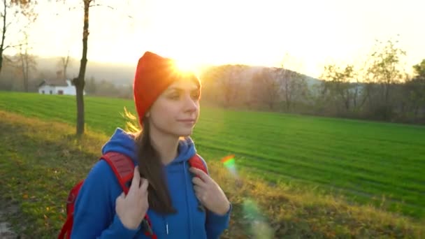 Mujer viajera con una mochila pasea por la carretera en el campo y admira el paisaje circundante — Vídeos de Stock