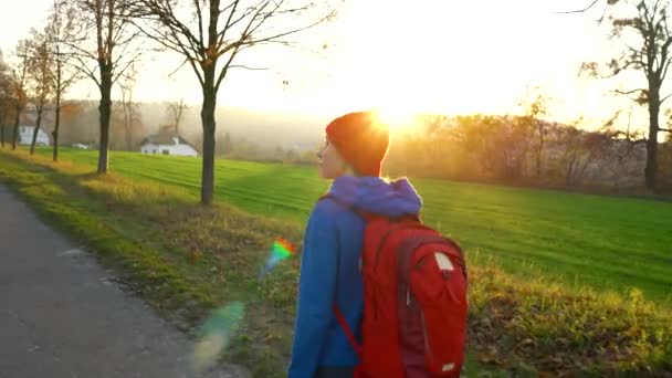 Kvinna resenären med en ryggsäck promenader på vägen i landsbygden och beundrar den omgivande landskapet — Stockvideo