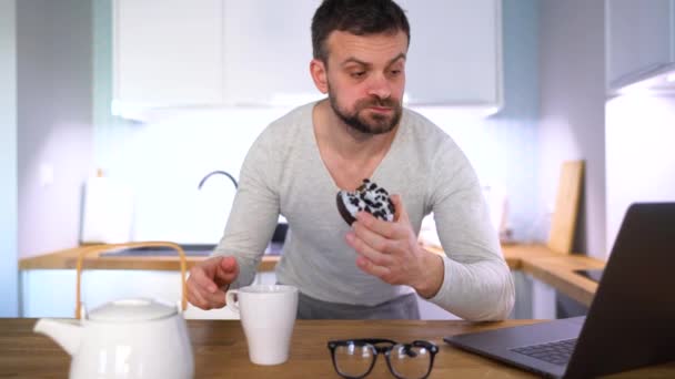 Bearded man having breakfast in the kitchen and using a laptop — Stock Video