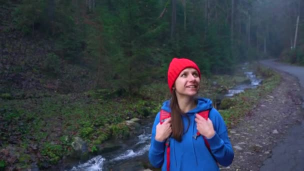 Nő utazó, egy hátizsák az út a hegyek, a folyó mentén sétál, és csodálja a környező táj — Stock videók