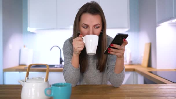 Кавказка завтракает на кухне и пользуется смартфоном — стоковое видео