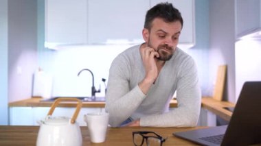 Mutfakta kahvaltı ve bir dizüstü bilgisayar kullanarak sakallı uykulu adam