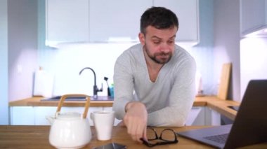 Mutfakta kahvaltı ve aynı zamanda bir dizüstü bilgisayar kullanarak sakallı uykulu adam