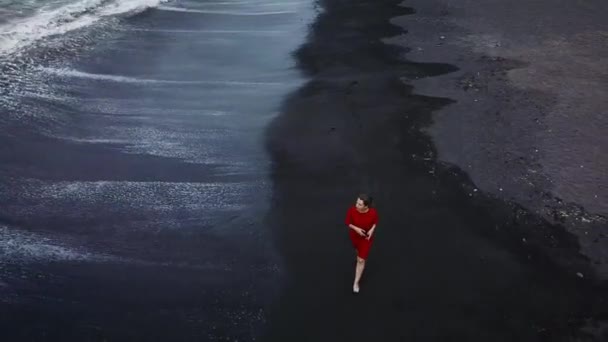 一个穿着红色礼服的女孩拿着黑色的沙子走在沙滩上的鸟图。特内里费岛, 加那利群岛, 西班牙 — 图库视频影像