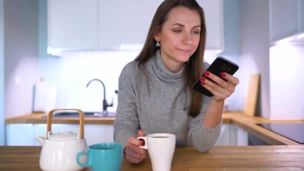 Mujer caucásica desayunando en la cocina y usando un smartphone — Vídeos de Stock