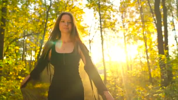 Menina bonita vestida de vestido preto caminha na floresta de outono e goza de bom tempo. Movimento lento — Vídeo de Stock