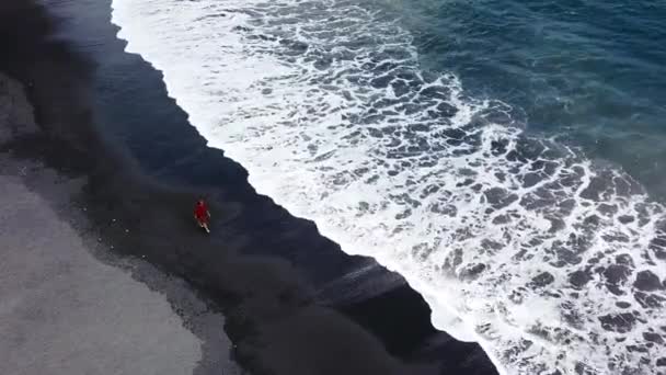 Veduta aerea di una ragazza in abito rosso che cammina sulla spiaggia con sabbia nera. Tenerife, Isole Canarie, Spagna — Video Stock