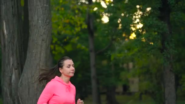 Gros plan d'une femme courant dans un parc d'automne au coucher du soleil. Mouvement lent — Video