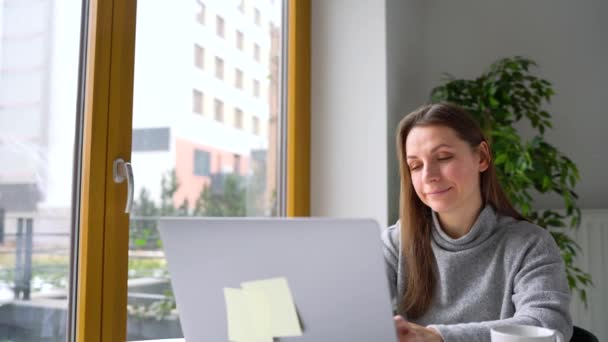 Schöne Frau sitzt zu Hause im Büro und arbeitet an einem Laptop — Stockvideo