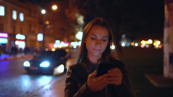 Mujer atractiva utiliza un teléfono inteligente mientras camina por las calles de la ciudad de la noche — Vídeos de Stock