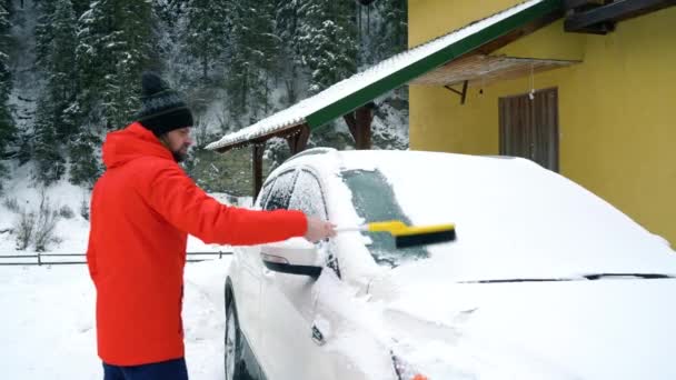 Člověk čistí auto od sněhu nedaleko jeho domu — Stock video