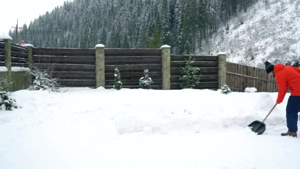 El hombre limpia la nieve con una pala en el patio de su casa — Vídeos de Stock