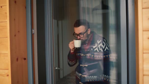 Hombre bebiendo té o café cerca de la ventana y mirando a través del vaso — Vídeo de stock