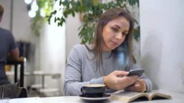 Güzel kadın bir kafede vaktini harcıyor: smartphone kullanarak ve kahve içme