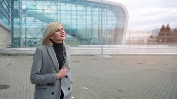 Menina loira rola uma mala perto do terminal do aeroporto. Movimento lento — Vídeo de Stock